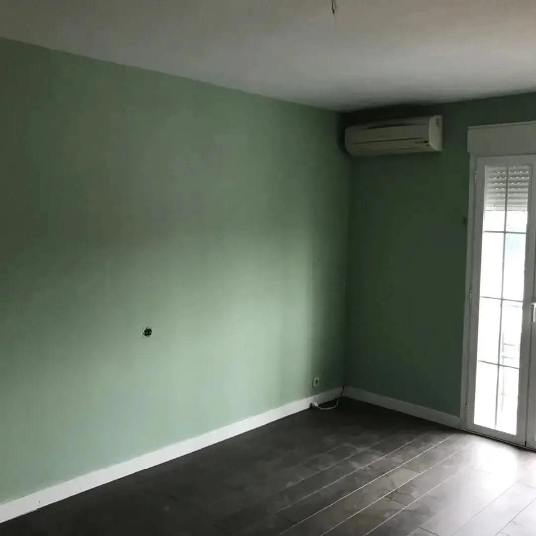 Habitación con paredes verdes y suelo oscuro tras reforma interior en vivienda de Madrid