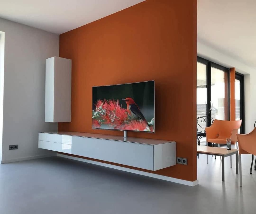 Salón moderno con pared naranja decorativa tras reforma integral en vivienda de Madrid