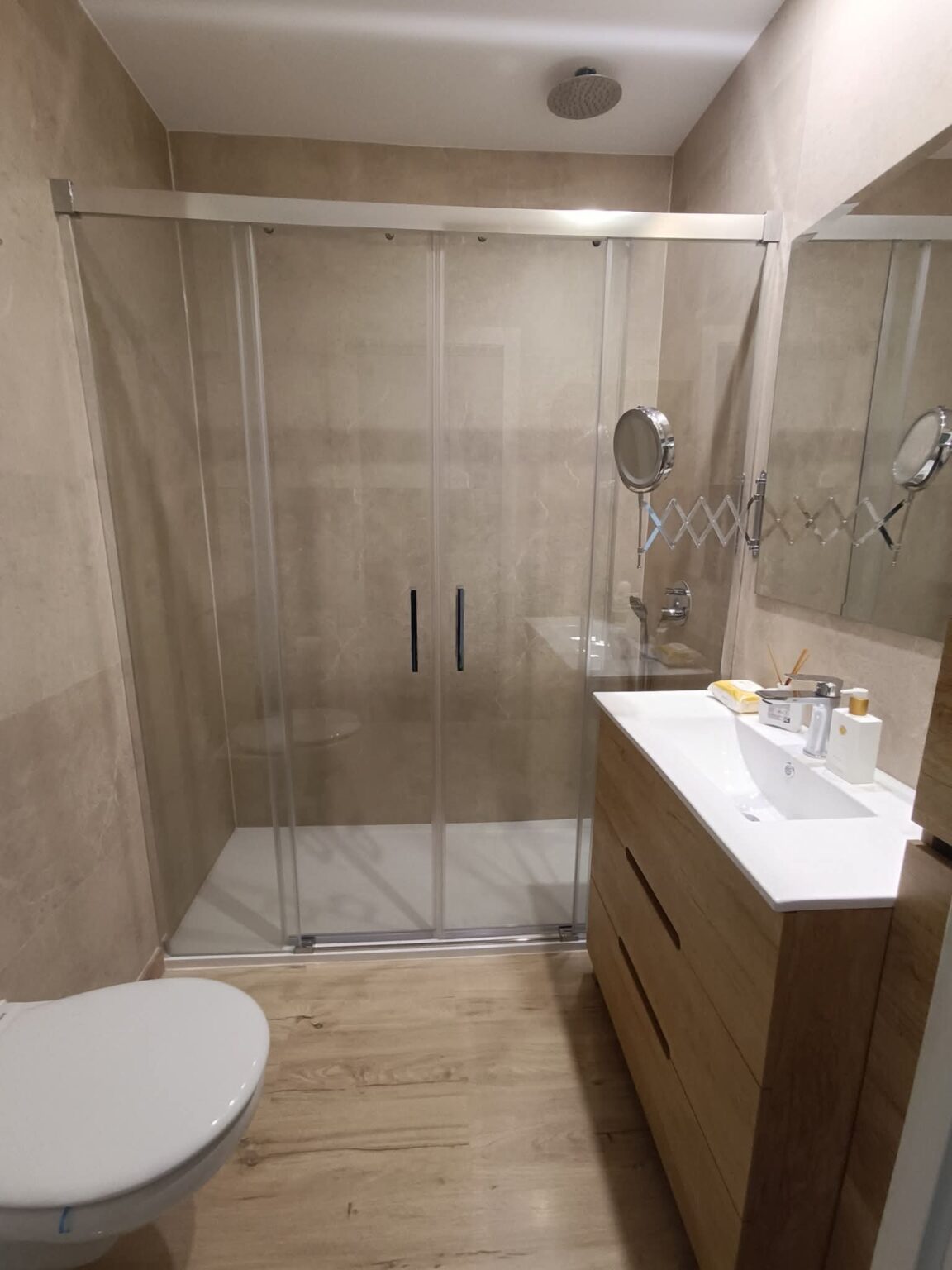 Baño reformado con ducha acristalada y muebles de madera en vivienda de Madrid